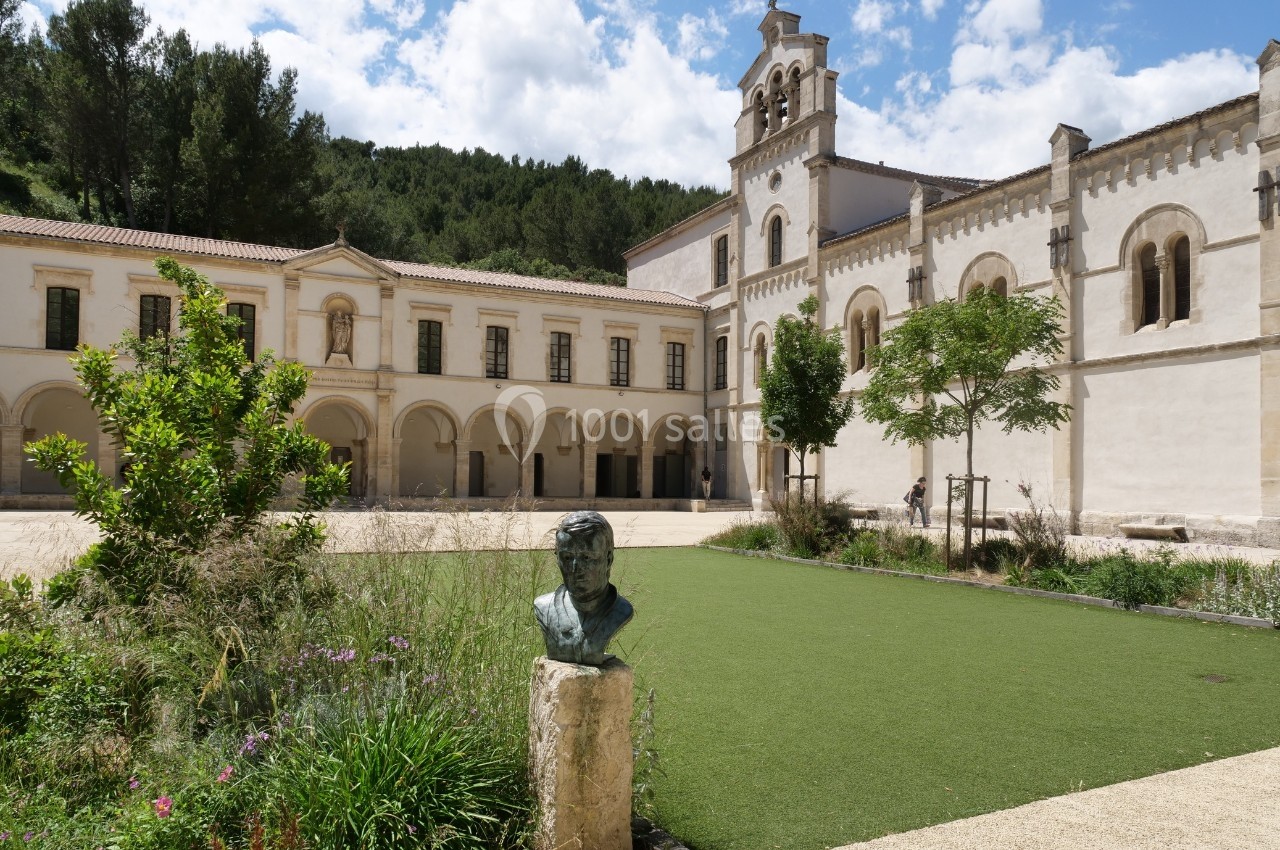 Cour d'un monastère avec jardin, statue en premier plan et bâtiment historique en arrière-plan sous un ciel dégagé.