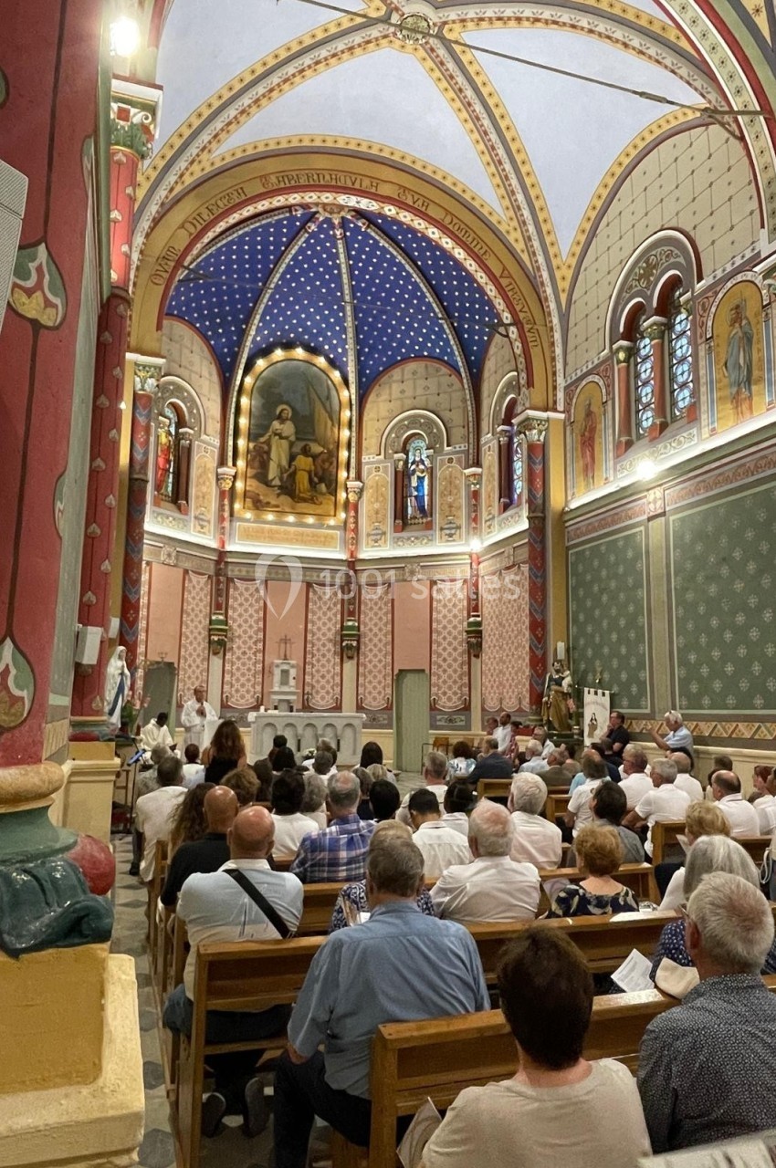 Intérieur d'une église avec des fidèles assis, ornée de fresques colorées, vitraux et voûtes décorées.