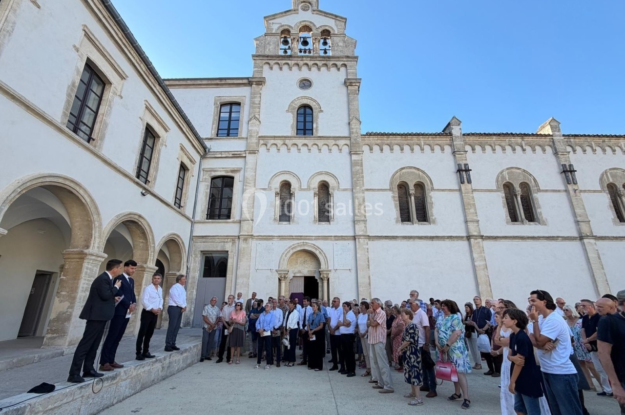 Un groupe de personnes rassemblées devant un bâtiment historique blanc sous un ciel dégagé.