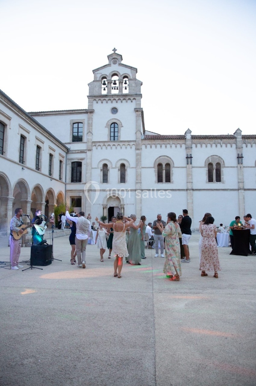 Groupe de personnes dansant en plein air dans la cour d'un bâtiment historique blanc par temps clair.