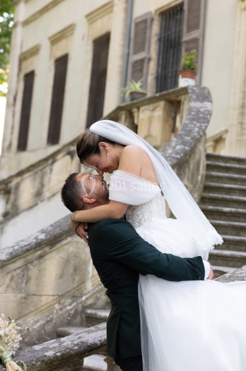 Un couple de mariés s'enlace sur un escalier en pierre devant un bâtiment ancien.