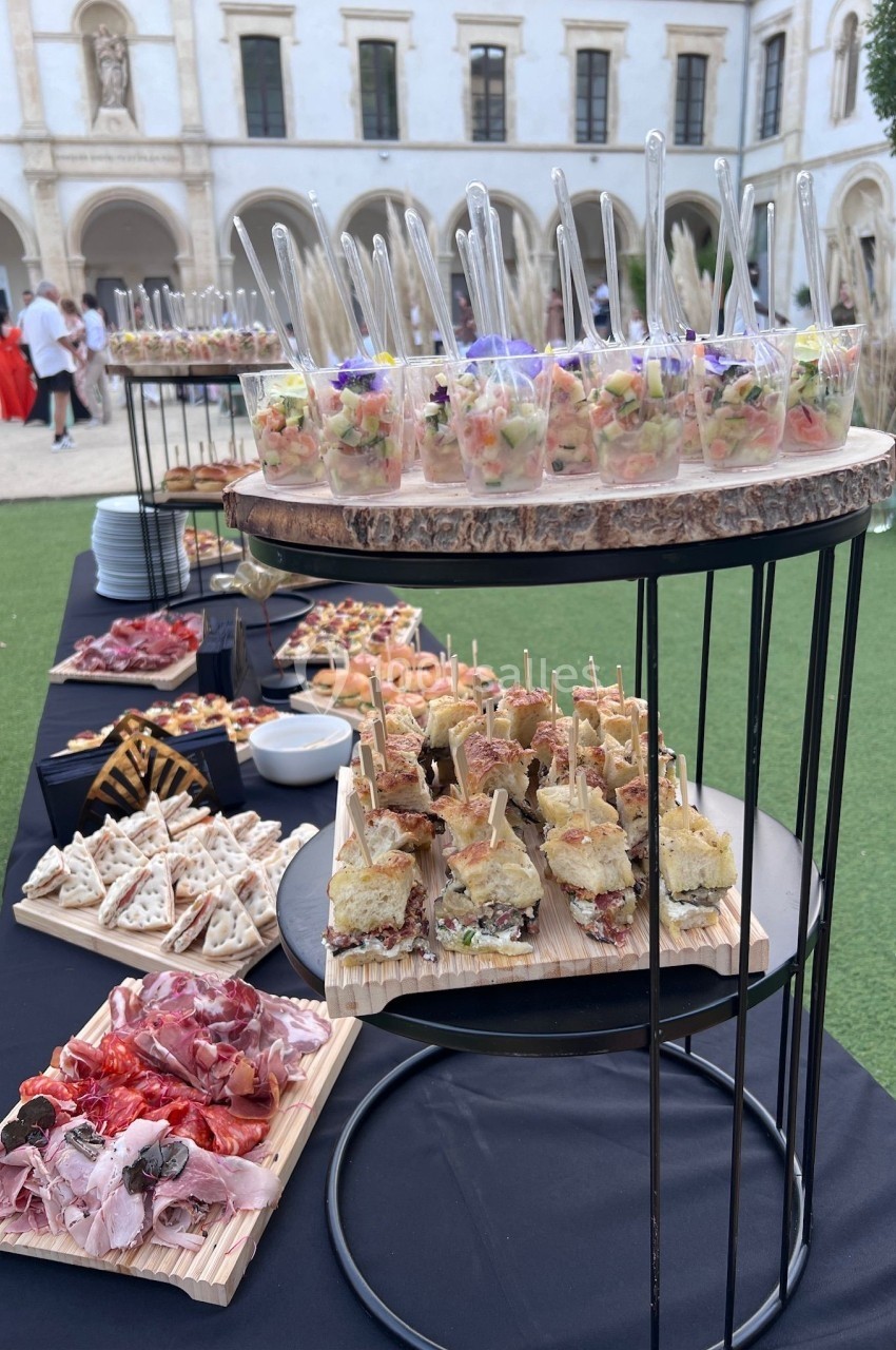 Buffet en plein air avec verrines, sandwichs et charcuterie, installé dans une cour avec bâtiment historique en arrière-plan.