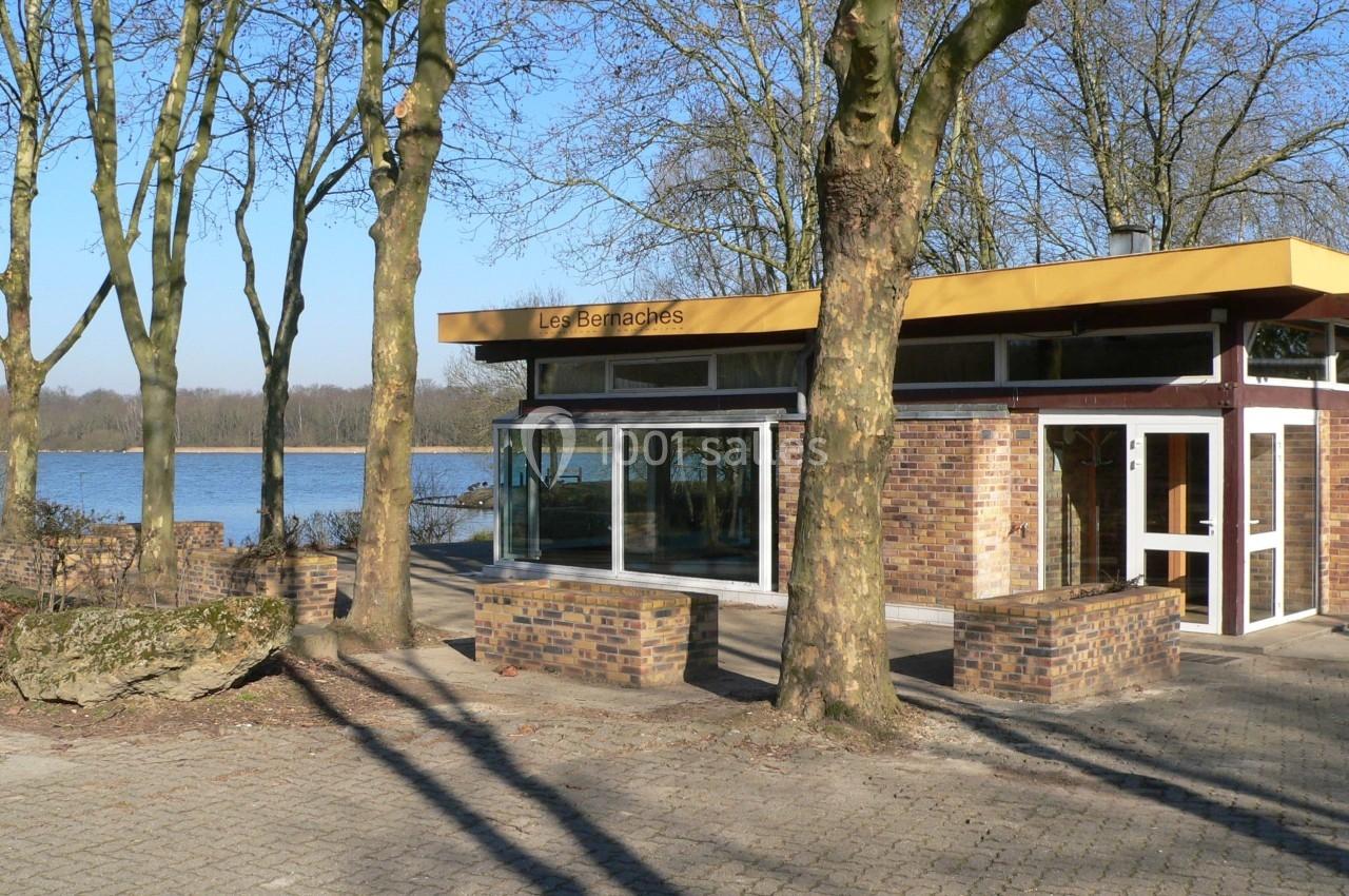 Bâtiment en briques avec de grandes baies vitrées, entouré d'arbres, près d'un lac sous un ciel dégagé.