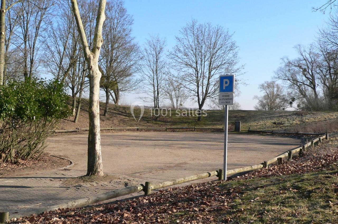 Parking vide en plein air entouré d'arbres en hiver, avec un panneau indiquant une zone de stationnement.
