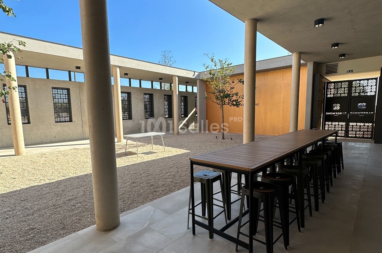 Cour intérieure moderne avec tables hautes, tabourets, sol en gravier et murs ornés de motifs ajourés.