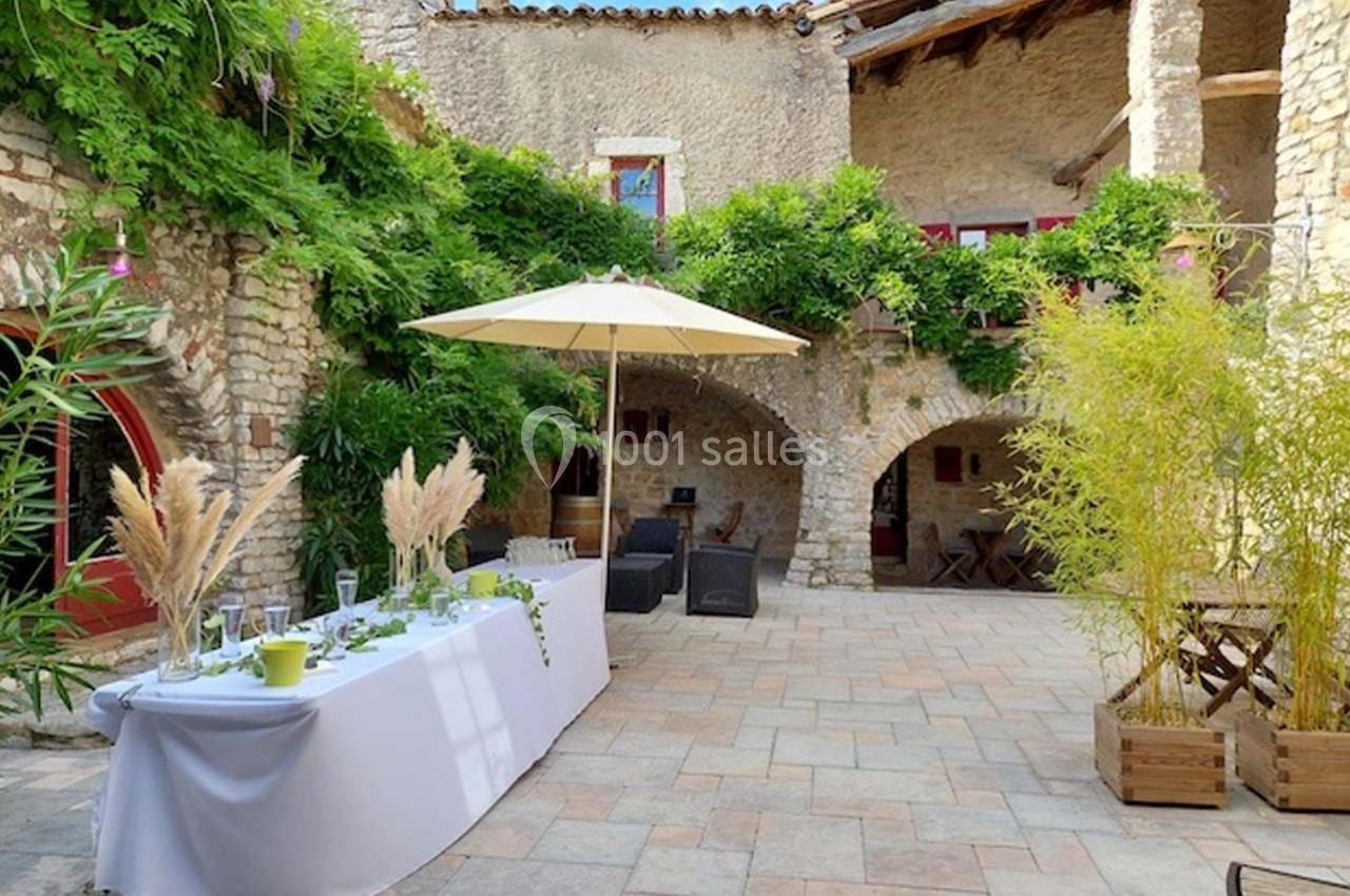 Cour en pierre avec table dressée sous un parasol, entourée de végétation et d'arches en pierre.