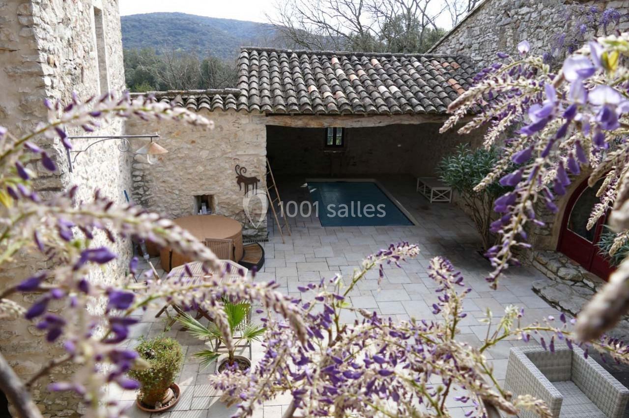 Cour intérieure en pierre avec piscine couverte, mobilier de jardin et glycine en fleurs au premier plan.