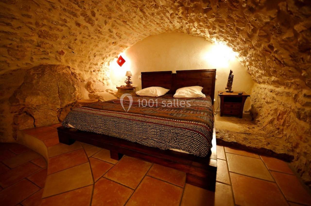 Chambre avec lit double dans une pièce voûtée en pierre, éclairée par des lampes chaleureuses et un sol en carrelage.