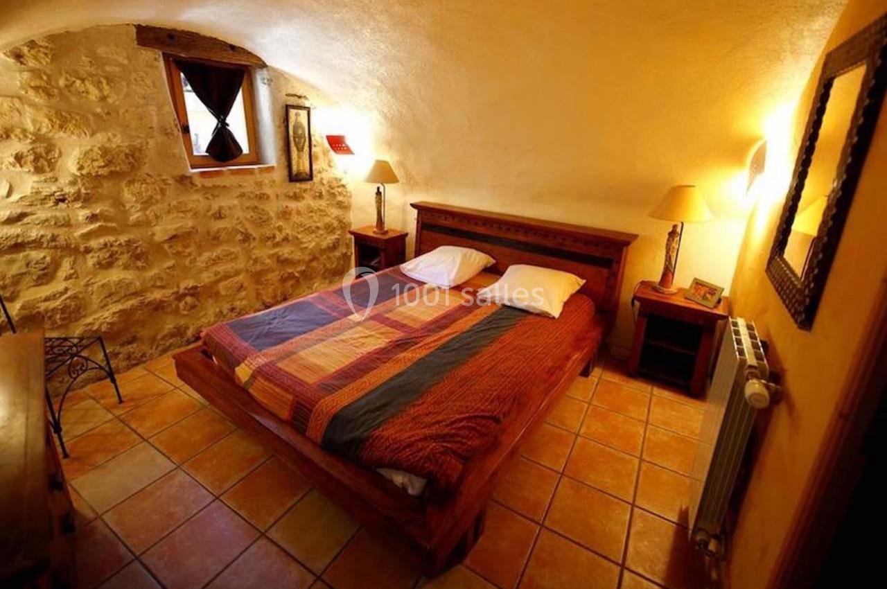 Chambre avec murs en pierre, lit double, lampes de chevet, sol en carrelage et petite fenêtre avec rideaux.