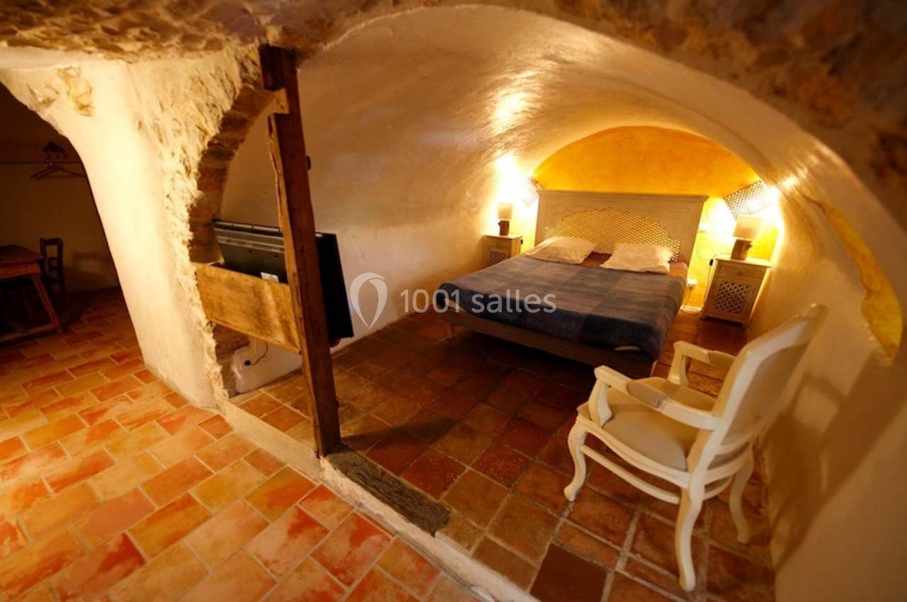 Chambre voûtée avec lit double, fauteuil blanc, éclairage chaleureux et sol en carreaux de terre cuite.