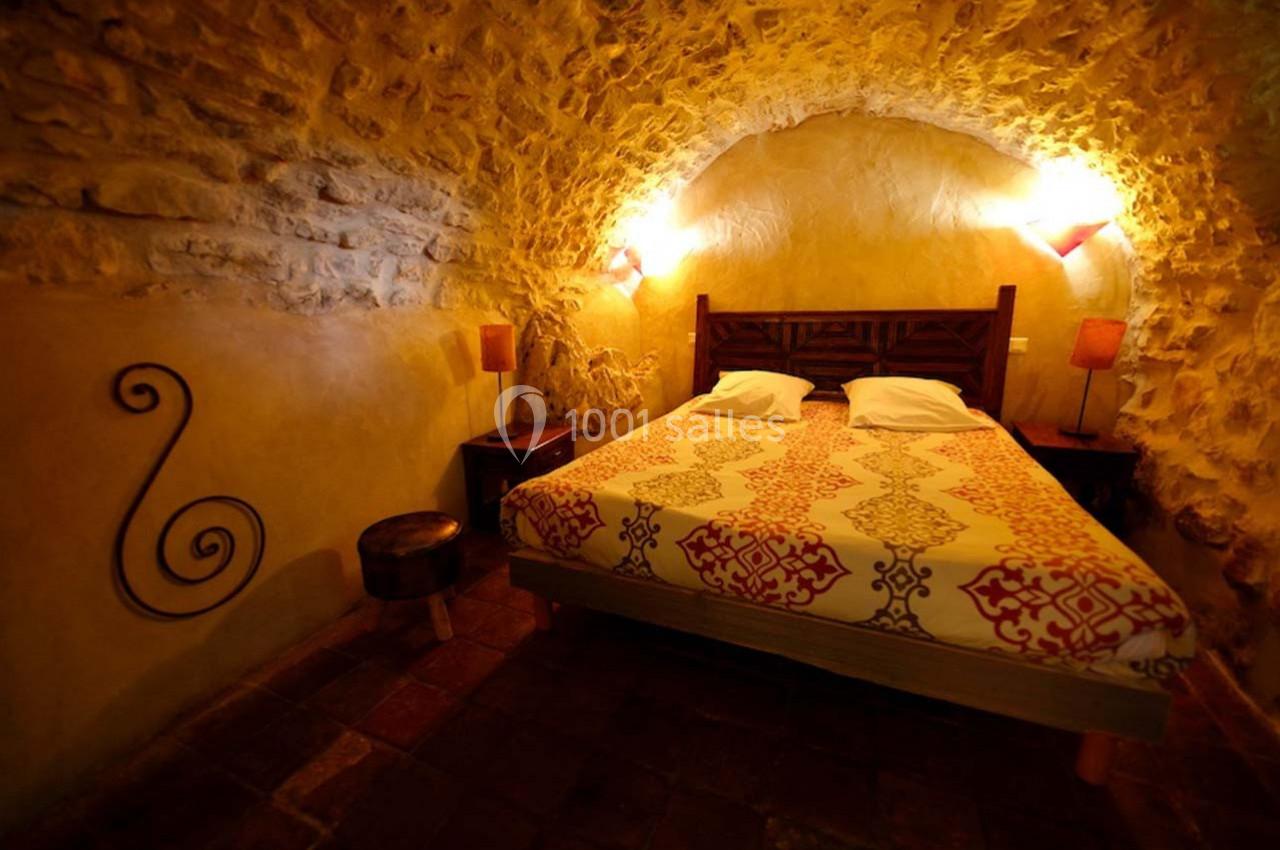 Chambre rustique avec murs en pierre, lit double, éclairage tamisé et décoration chaleureuse.