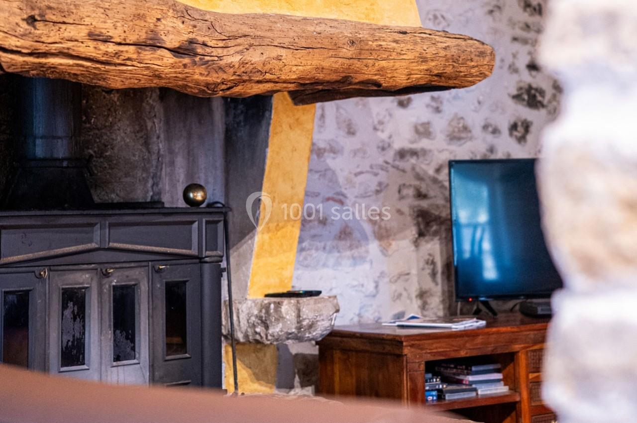 Cheminée rustique en pierre avec poutre en bois, poêle noir et téléviseur sur un meuble en bois à droite.