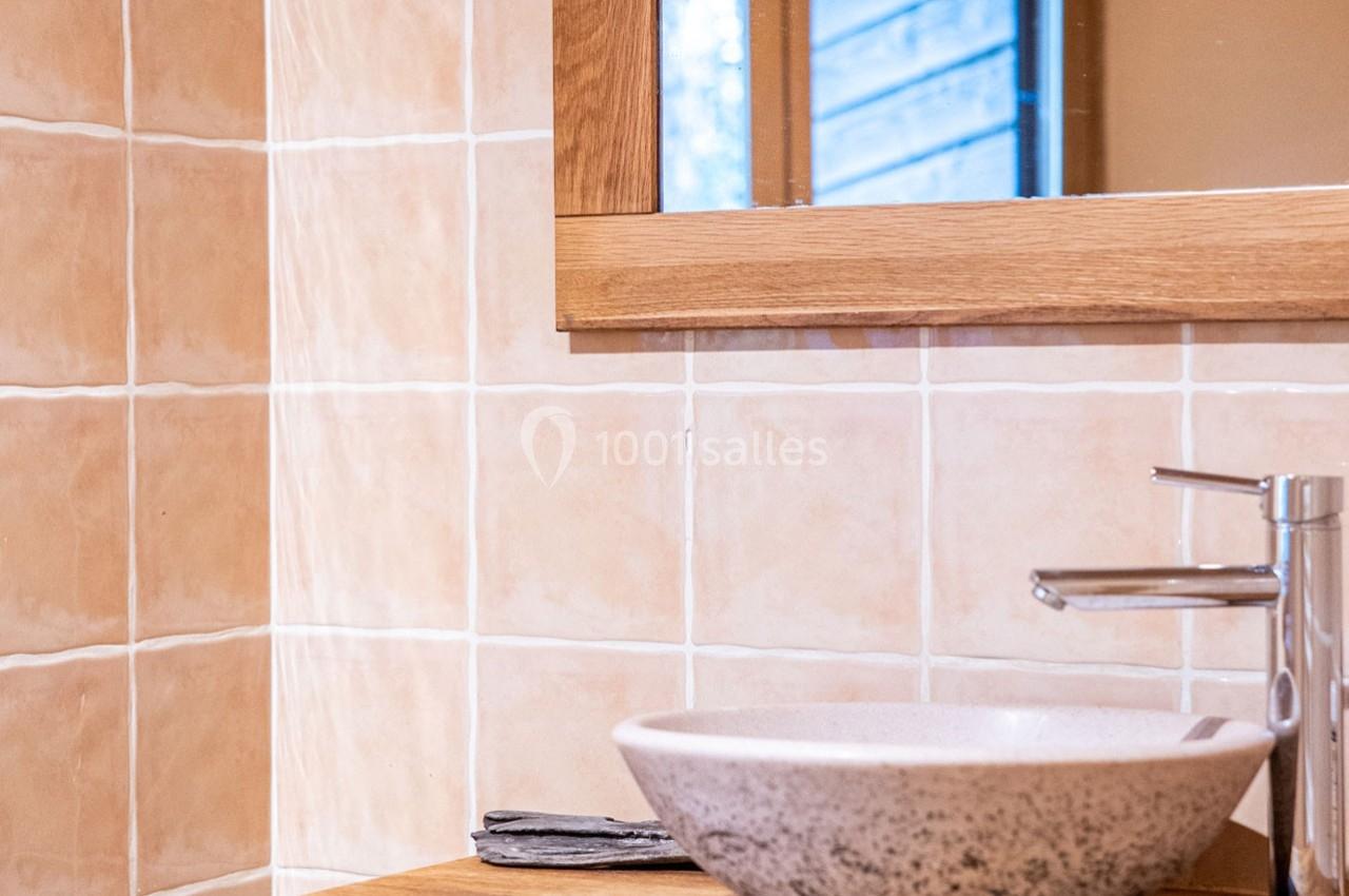 Lavabo en céramique posé sur un plan en bois, avec un robinet métallique et un miroir encadré de bois.