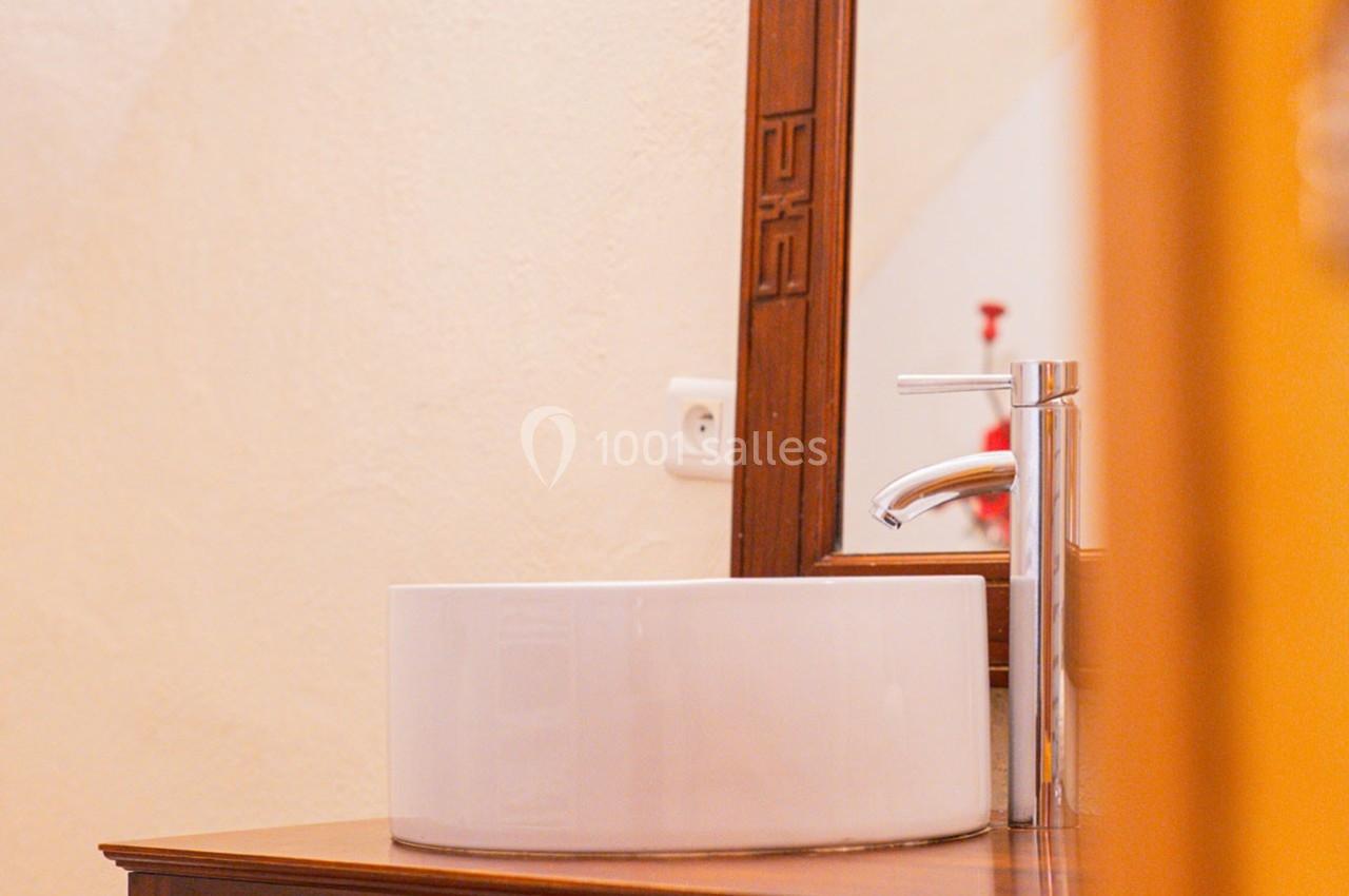 Lavabo blanc rond posé sur un meuble en bois, avec un robinet chromé et un miroir en arrière-plan.