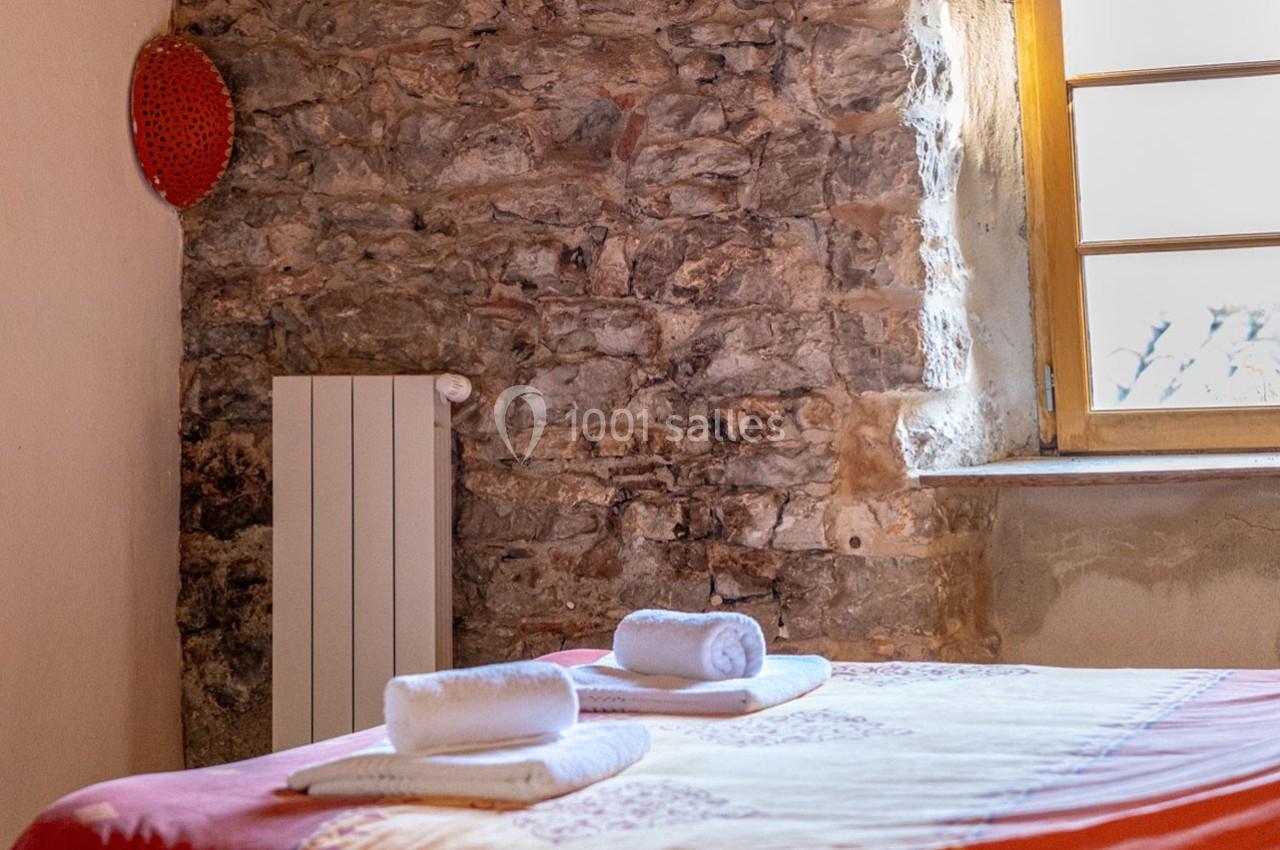 Lit avec serviettes roulées dans une chambre aux murs en pierre apparente et fenêtre laissant entrer la lumière naturelle.