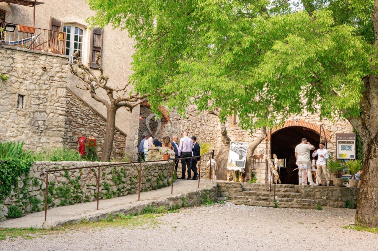Entrée d'un bâtiment en pierre avec des visiteurs, entourée d'arbres et d'une rampe d'accès.