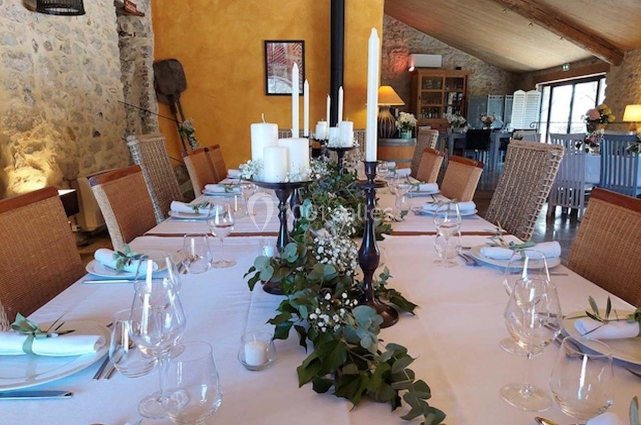 Table dressée avec une nappe blanche, décorée de bougies et de feuillage, dans une salle en pierre au style rustique.