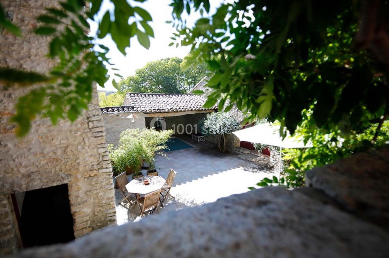 Cour ensoleillée avec table et chaises en bois, entourée de murs en pierre et de végétation.
