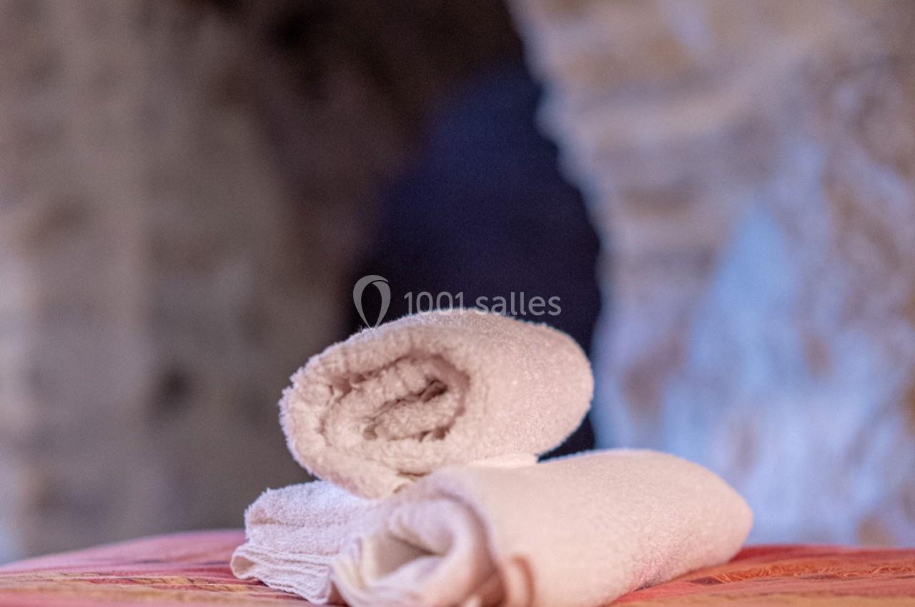 Deux serviettes blanches roulées posées sur une surface rose, avec un fond flou en pierre.