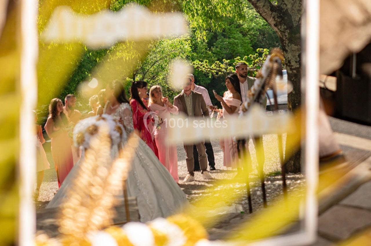 Un groupe de personnes en tenue de cérémonie, capturé à travers un reflet flou sous des arbres verdoyants.