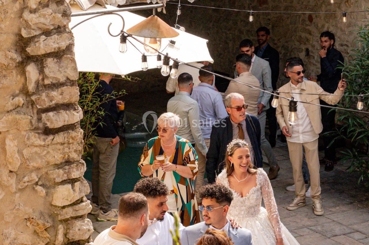 Des invités discutent et se déplacent dans une cour en pierre décorée de guirlandes lumineuses, lors d'une réception.