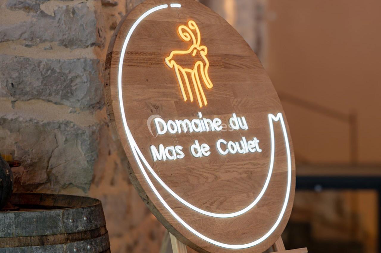 Panneau en bois rond avec un logo lumineux et l'inscription ’Domaine du Mas de Coulet’, posé sur un chevalet.