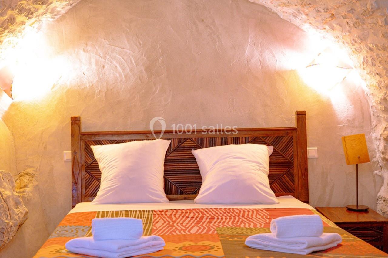 Lit double avec tête de lit en bois sculpté, draps blancs et serviettes pliées, dans une chambre aux murs en pierre.