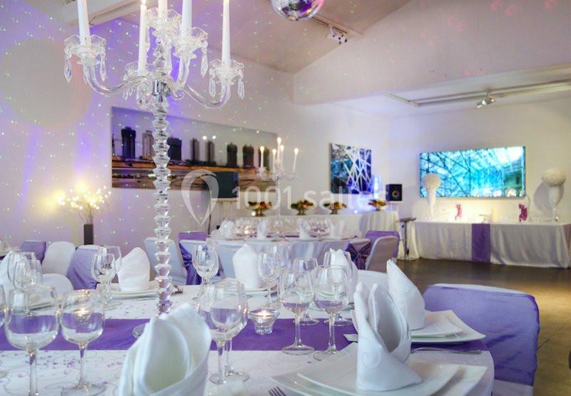 Salle de réception décorée avec des nappes violettes, chandeliers et tables dressées pour un événement festif.