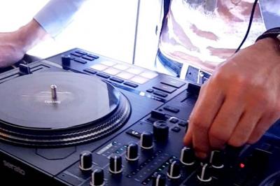 Un DJ mixant de la musique sur une table de mixage avec un ordinateur portable dans un environnement lumineux.