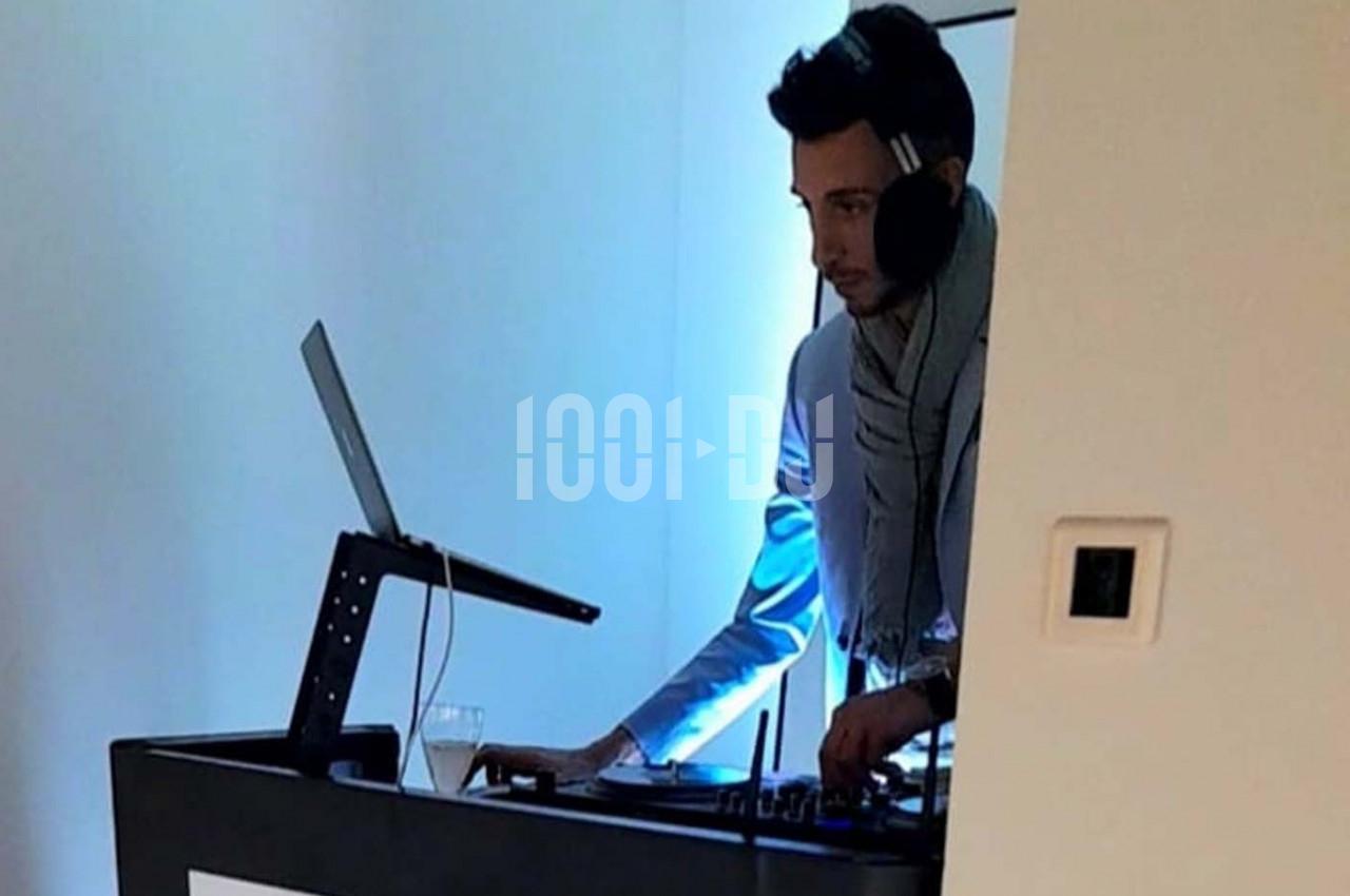 Un DJ mixant sur une table de mixage avec un ordinateur portable, dans une pièce éclairée par une lumière bleutée.