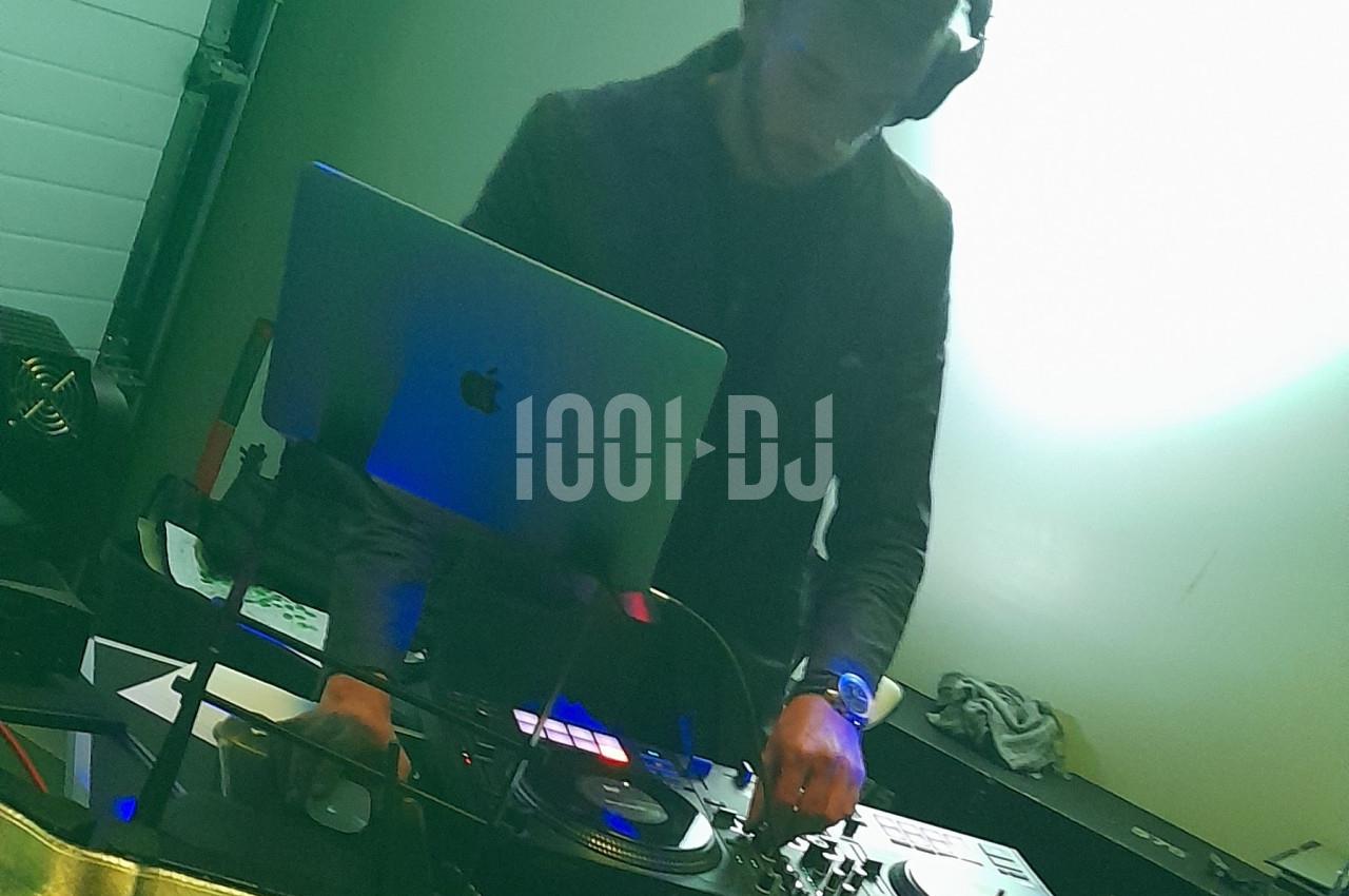 Un DJ mixant de la musique sur une table de mixage avec un ordinateur portable dans un environnement lumineux.