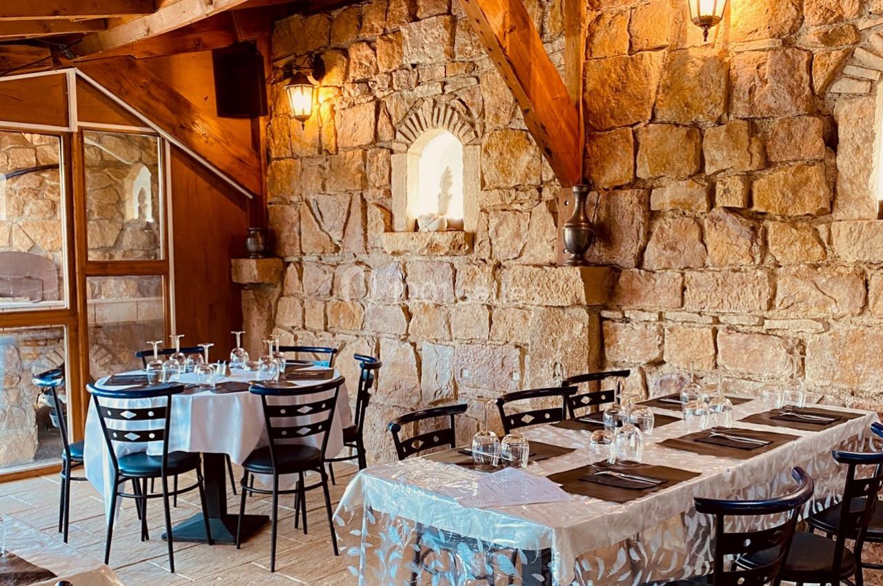 Salle de restaurant avec murs en pierre, tables dressées et éclairage chaleureux.