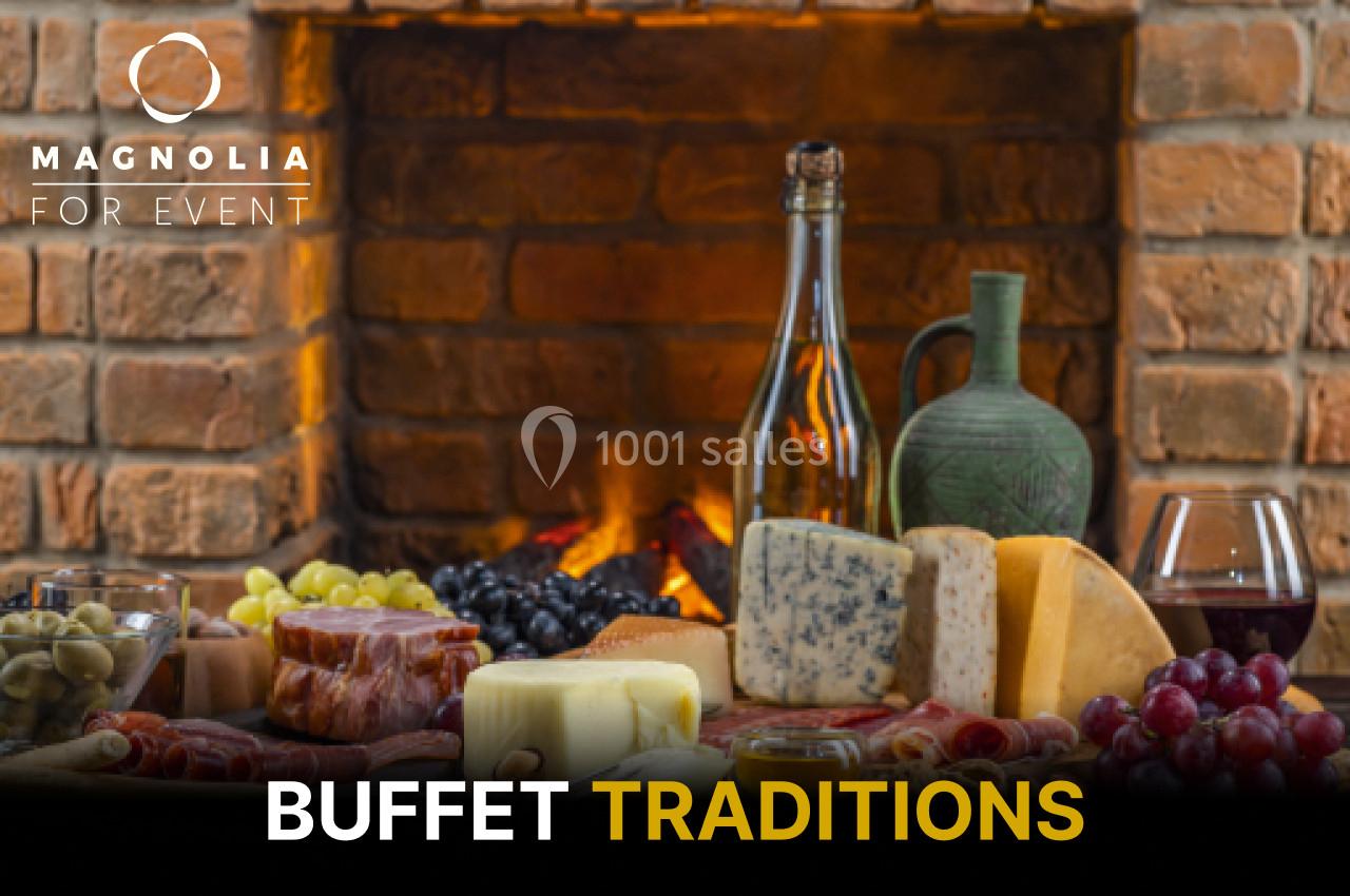 Plateau de fromages, charcuteries, fruits et pain devant une cheminée, accompagné de vin et d'une bouteille.