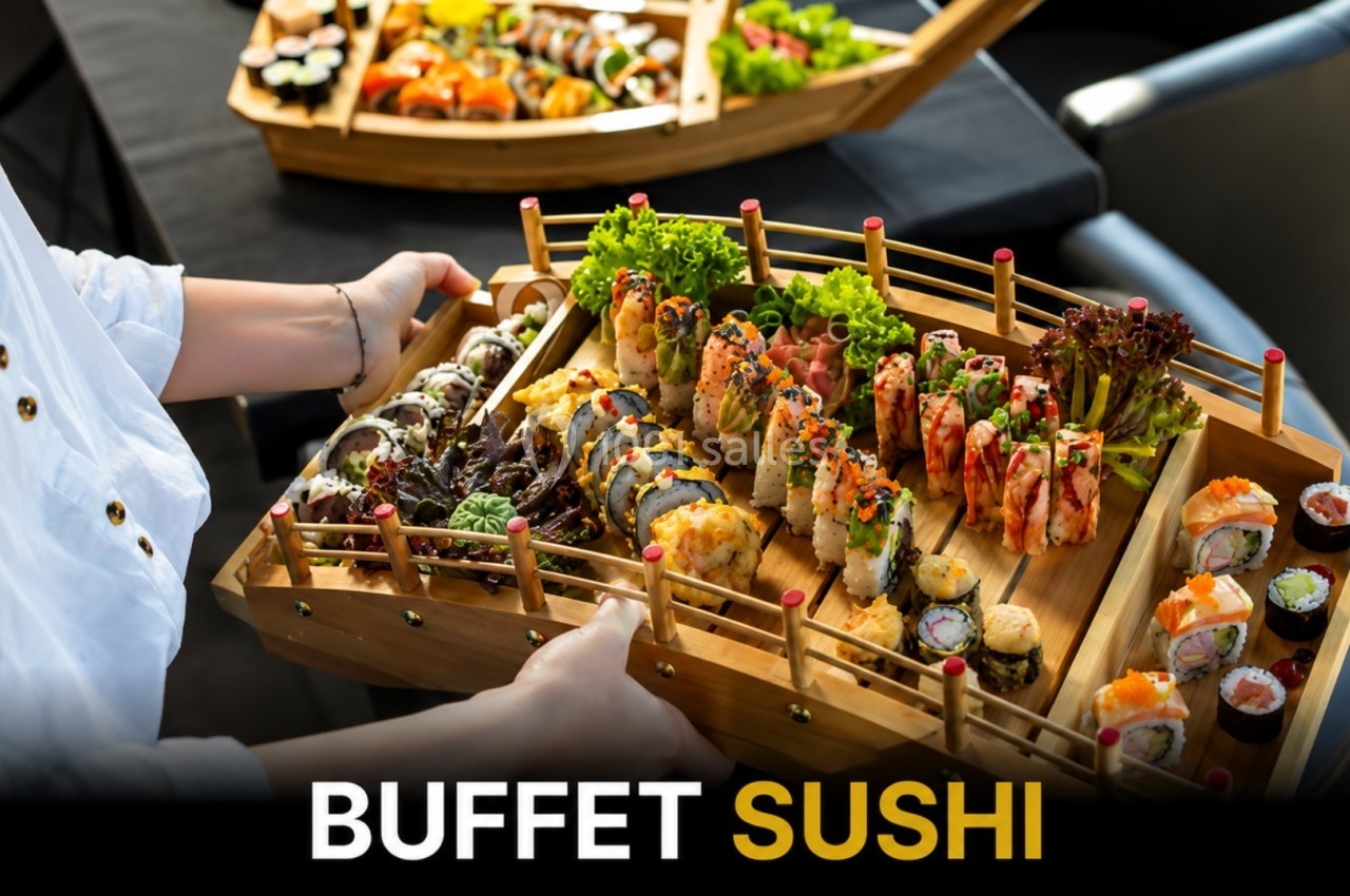 Plateau en bois rempli de sushis variés, makis et garnitures, tenu par une personne dans un restaurant.