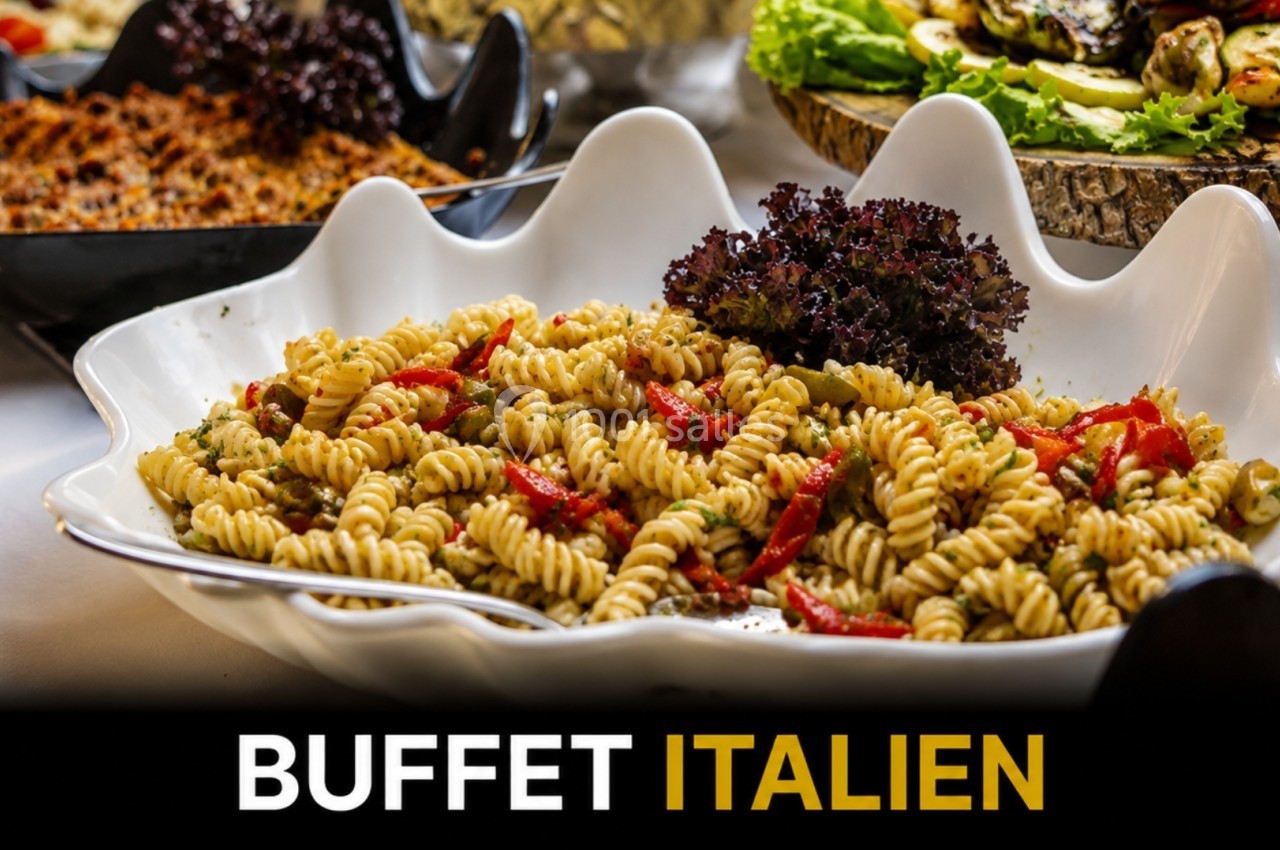 Assiette de pâtes fusilli garnies de légumes et herbes, présentée sur un buffet avec d'autres plats variés.
