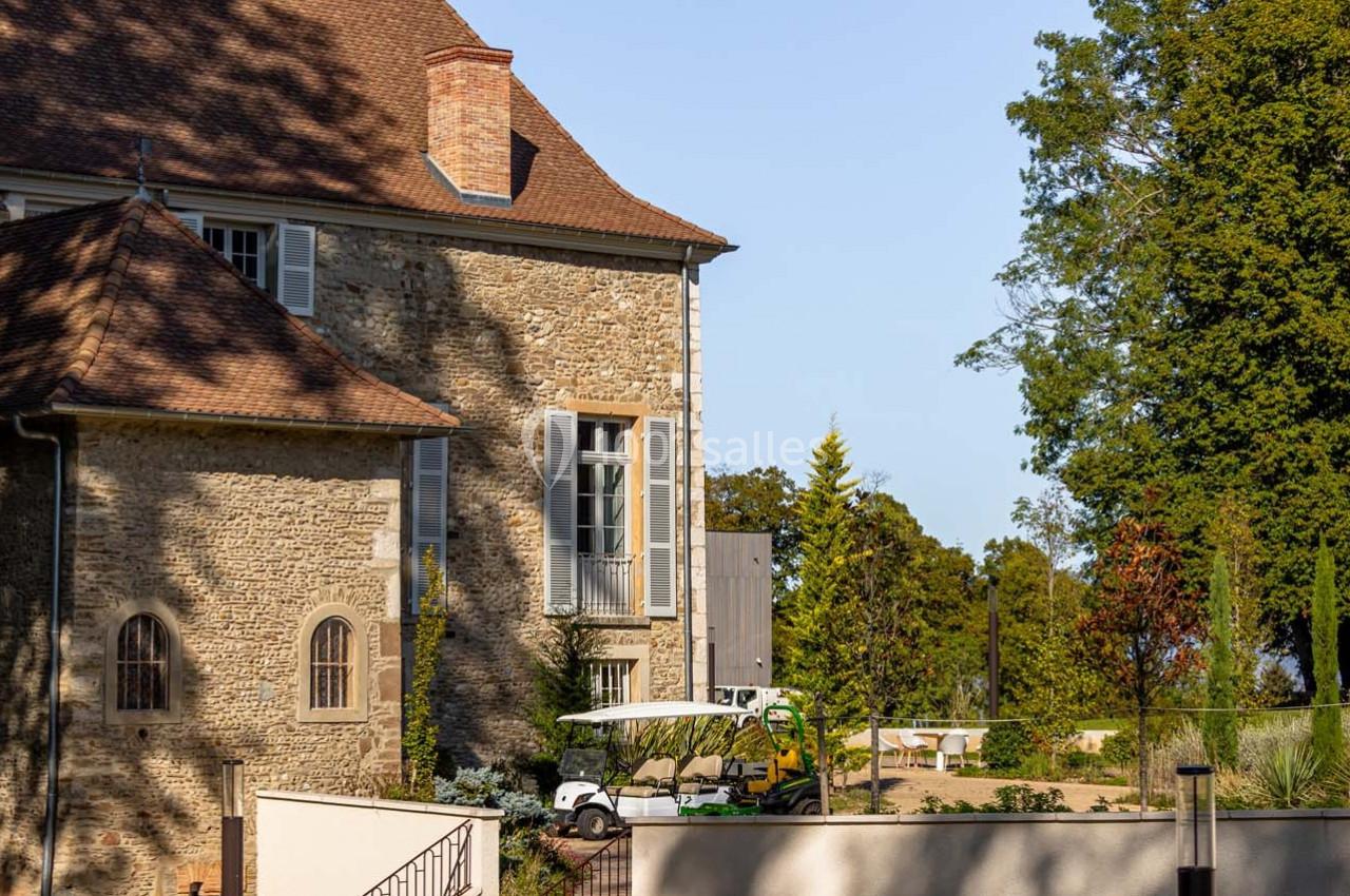 Façade en pierre d'un bâtiment ancien avec un toit en tuiles, entouré de végétation et d'une petite voiturette blanche.