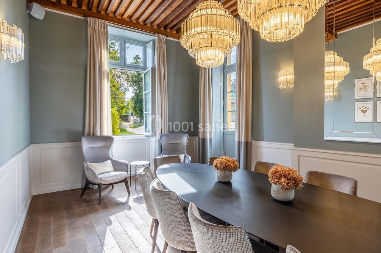 Salle à manger lumineuse avec table noire, chaises claires, lustres élégants et grandes fenêtres donnant sur un jardin.