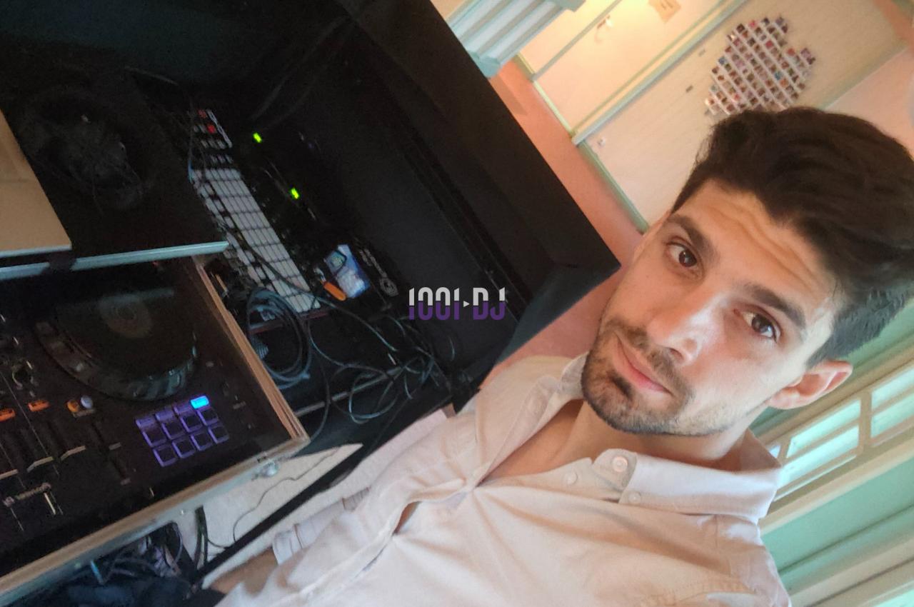 Un homme en chemise blanche se tient près d'une table de mixage dans un espace intérieur lumineux.