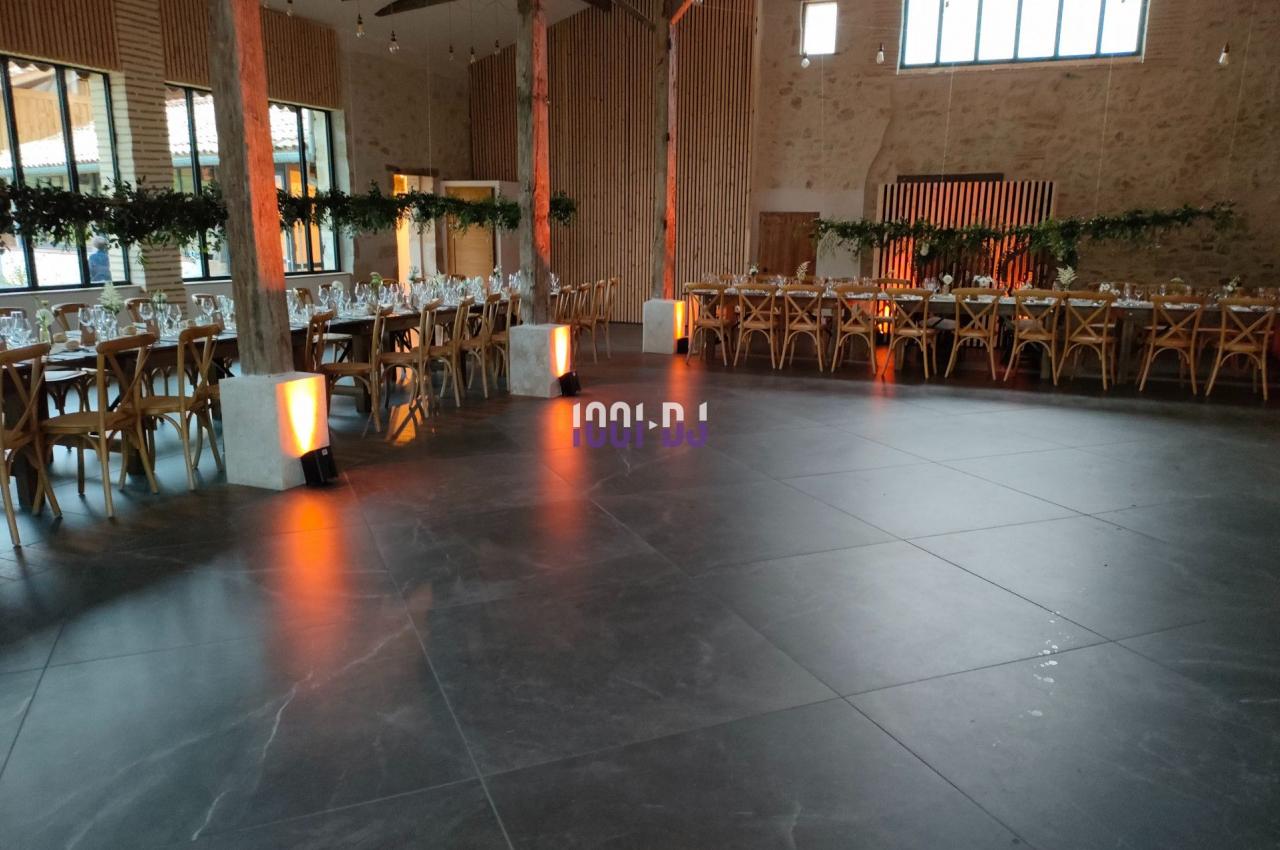 Salle de réception spacieuse avec tables dressées, chaises en bois et éclairage tamisé près des piliers.
