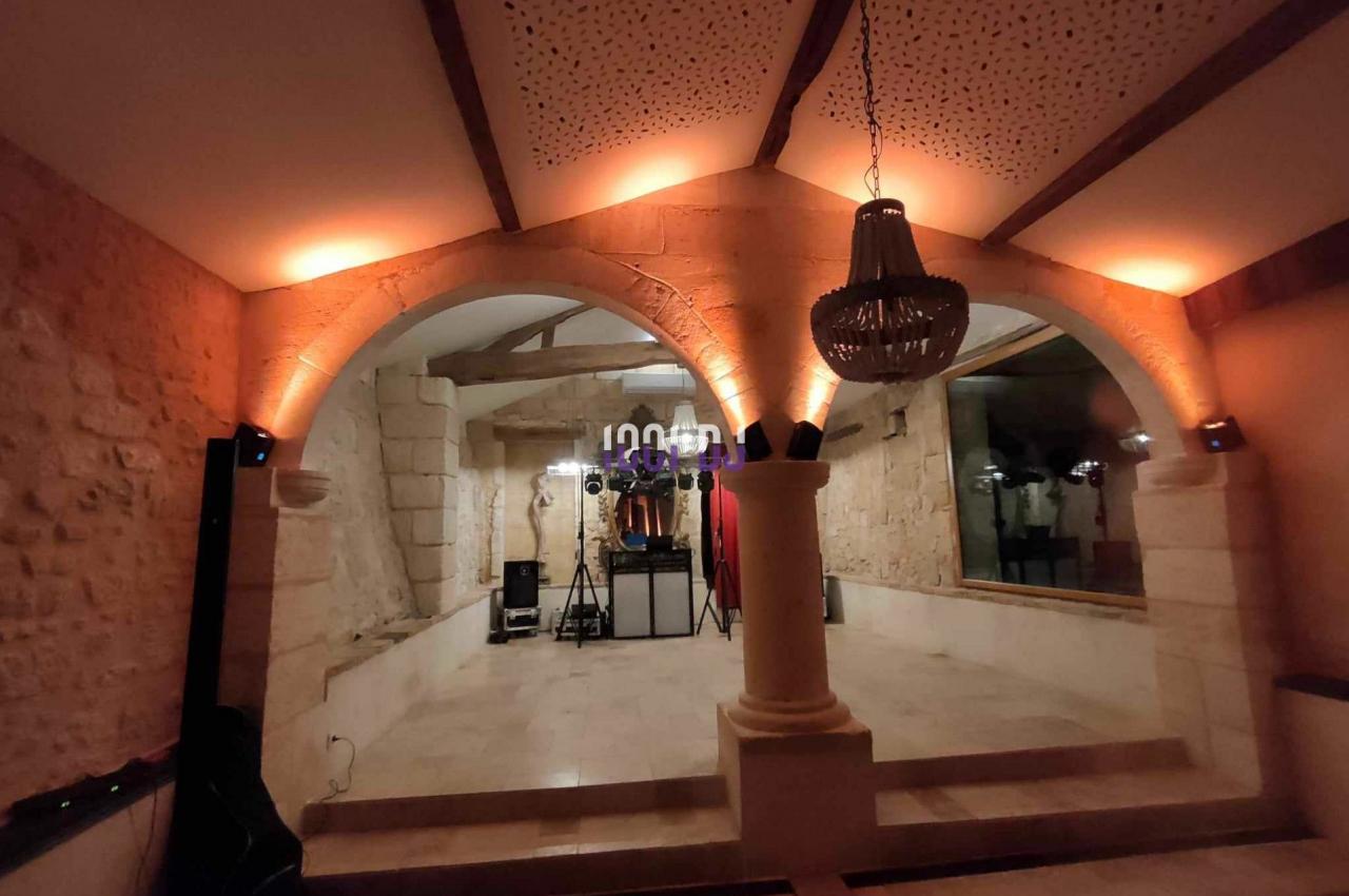 Salle voûtée en pierre avec éclairage tamisé, lustre suspendu et équipement audio installé au fond.