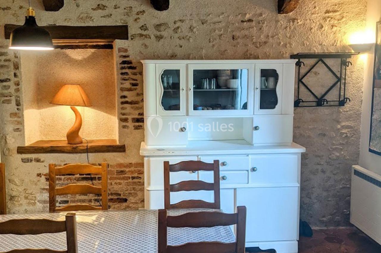 Buffet blanc dans une salle à manger rustique avec murs en pierre, table en bois et lampe sur une étagère murale.