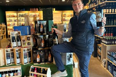 Miniature Location salle La Madeleine (Nord) - Salle V and B La Madeleine #6 Un homme pose dans un magasin de boissons, tenant deux bouteilles devant un présentoir de bières variées.