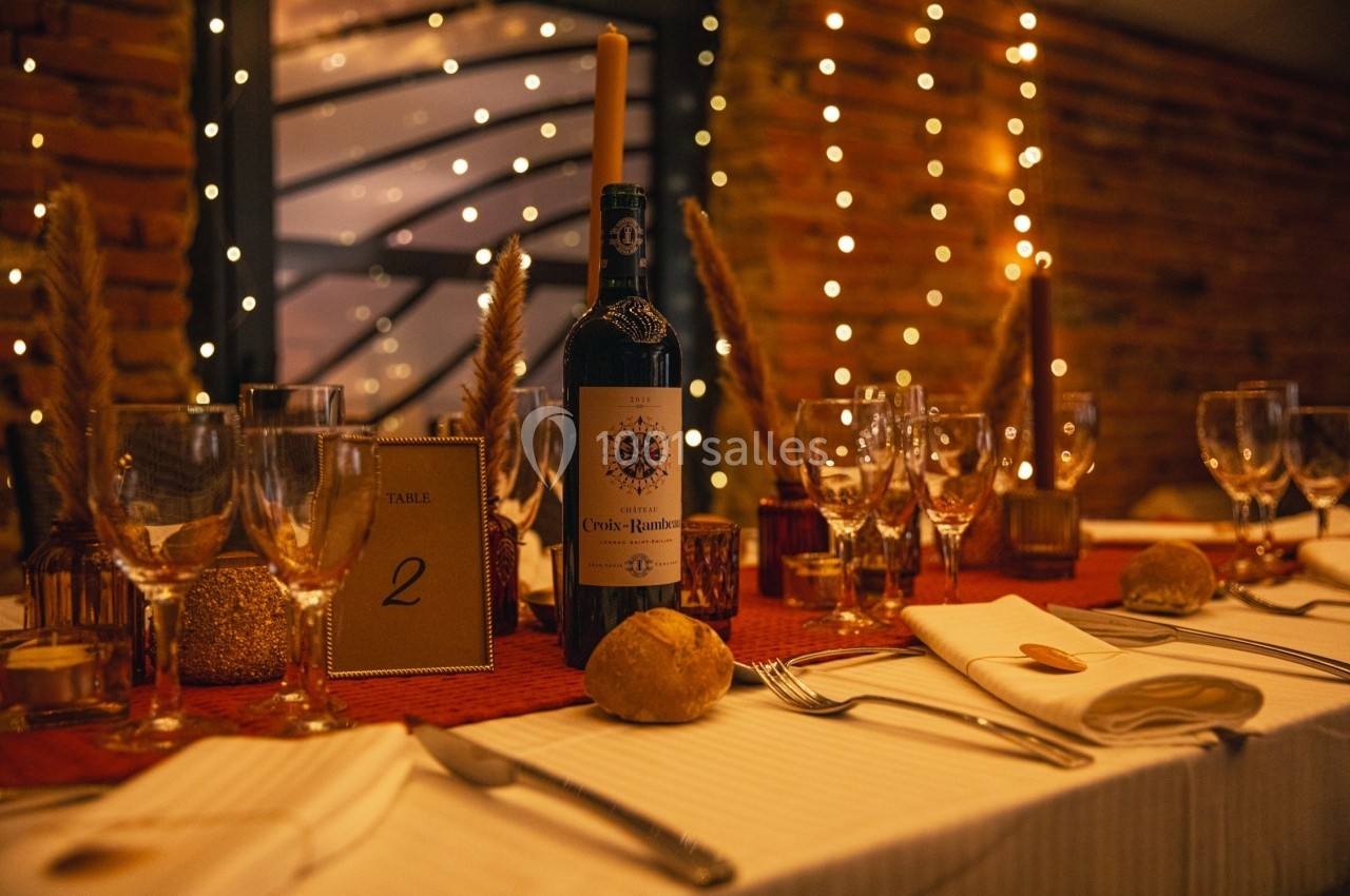 Table élégamment dressée avec bougies, bouteille de vin, verres et décorations lumineuses dans une ambiance chaleureuse.