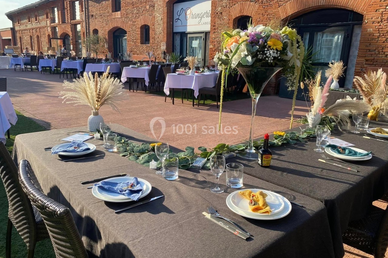 Tables dressées pour un événement en extérieur, avec nappes sombres, vaisselle élégante et décorations florales.