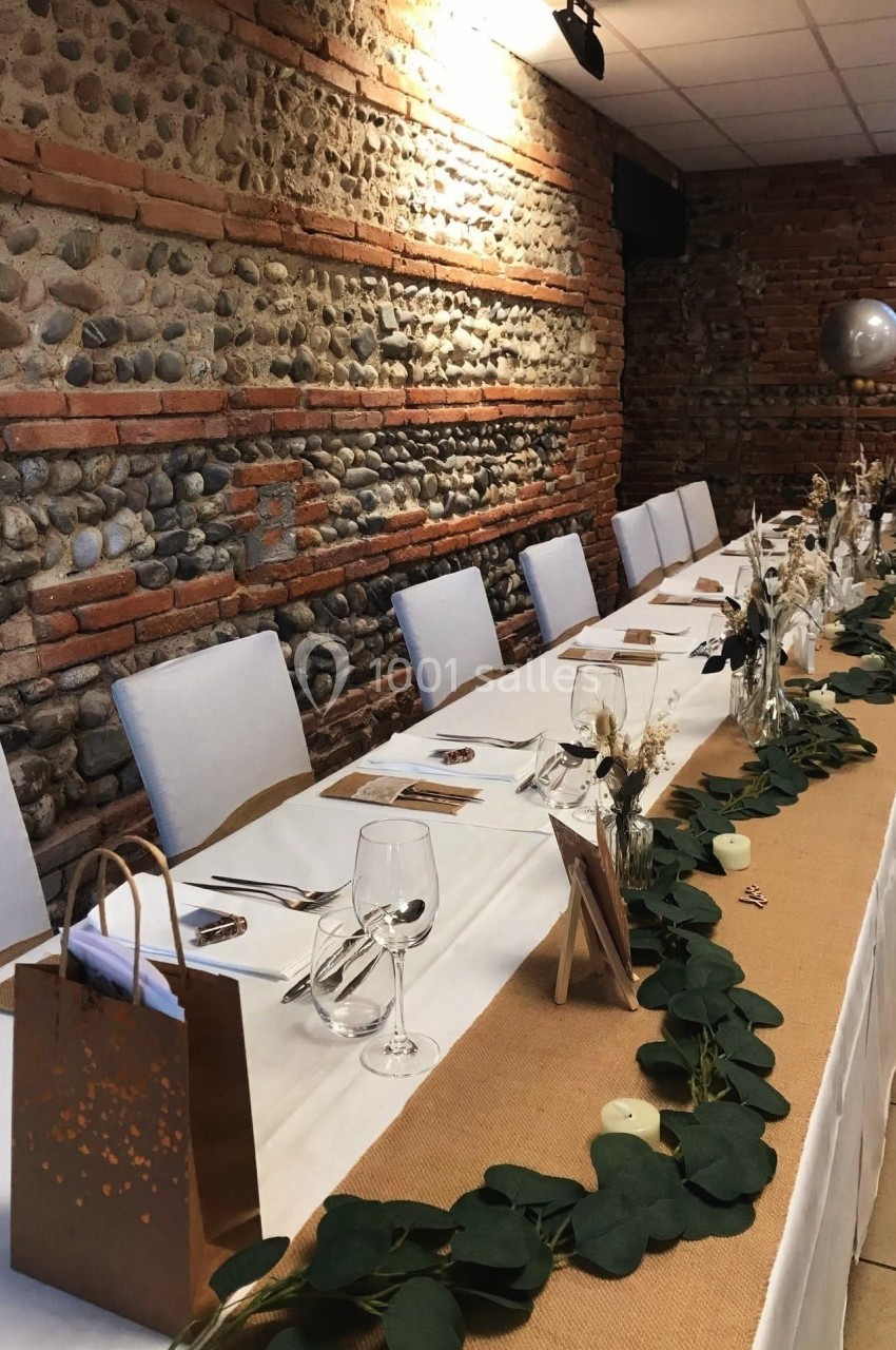 Table décorée pour un événement, avec nappes blanches, chemin de table en jute, feuillage et décorations élégantes.