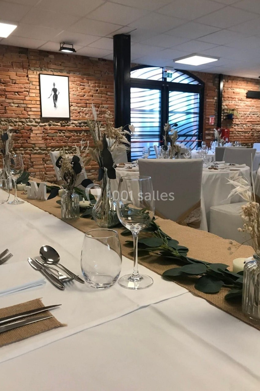 Salle de réception décorée avec des tables dressées, ornées de fleurs séchées et de chemins de table en jute.