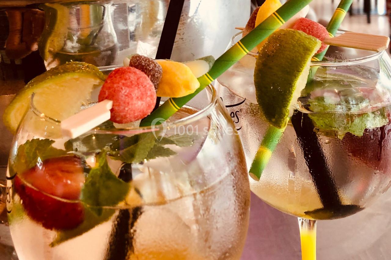 Deux verres de cocktail garnis de fruits frais, glaçons, feuilles de menthe et pailles colorées.