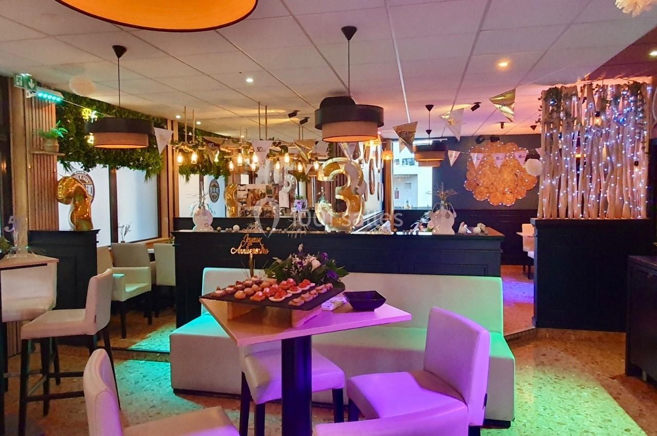 Salle de réception décorée avec des guirlandes lumineuses, des ballons dorés et des tables dressées pour un événement.