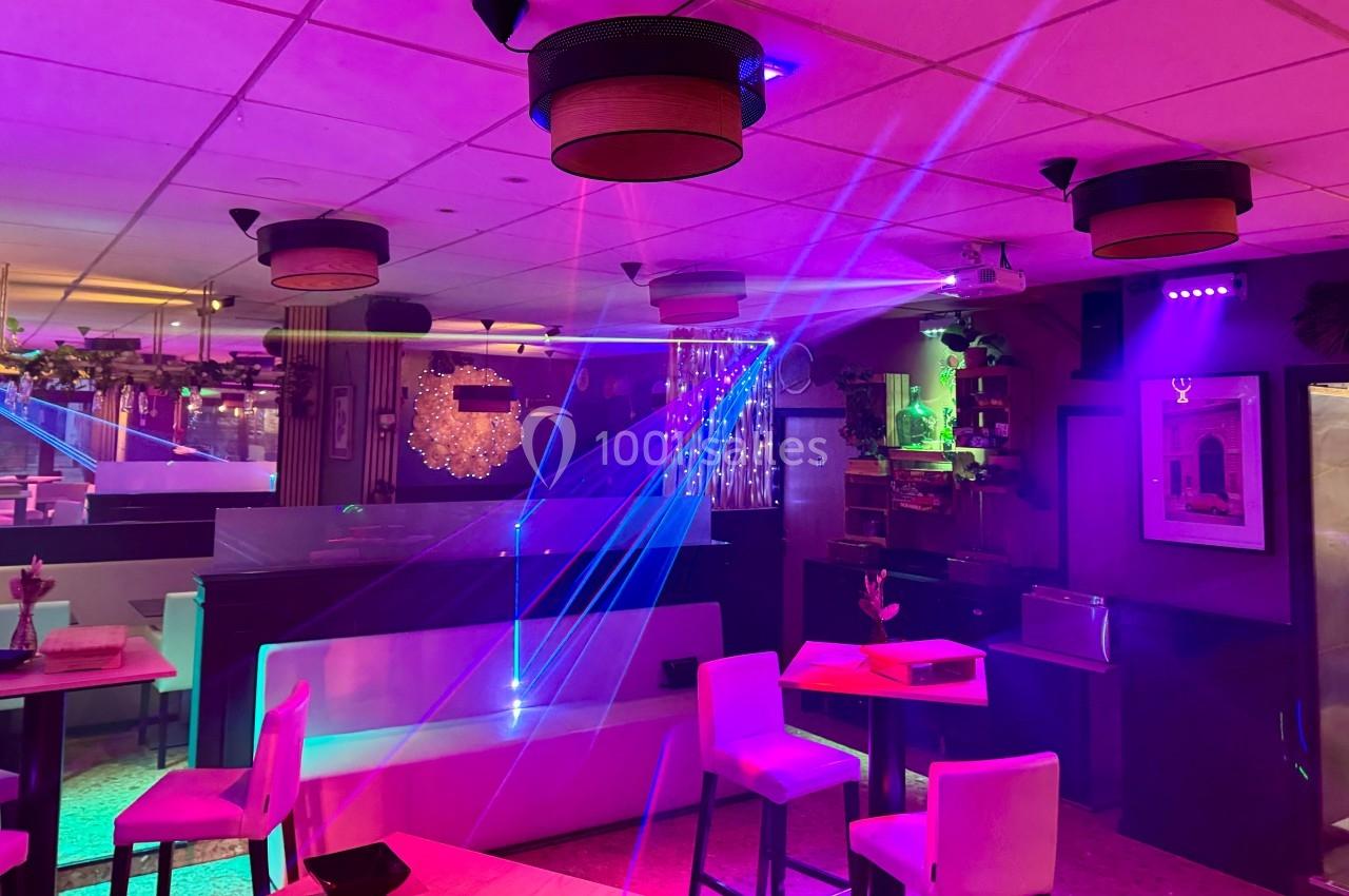 Salle de restaurant avec éclairage coloré et lasers, tables dressées et ambiance festive.