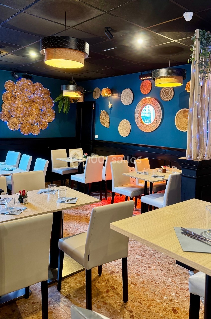 Salle de restaurant moderne avec tables dressées, chaises blanches, décoration murale et éclairage chaleureux.